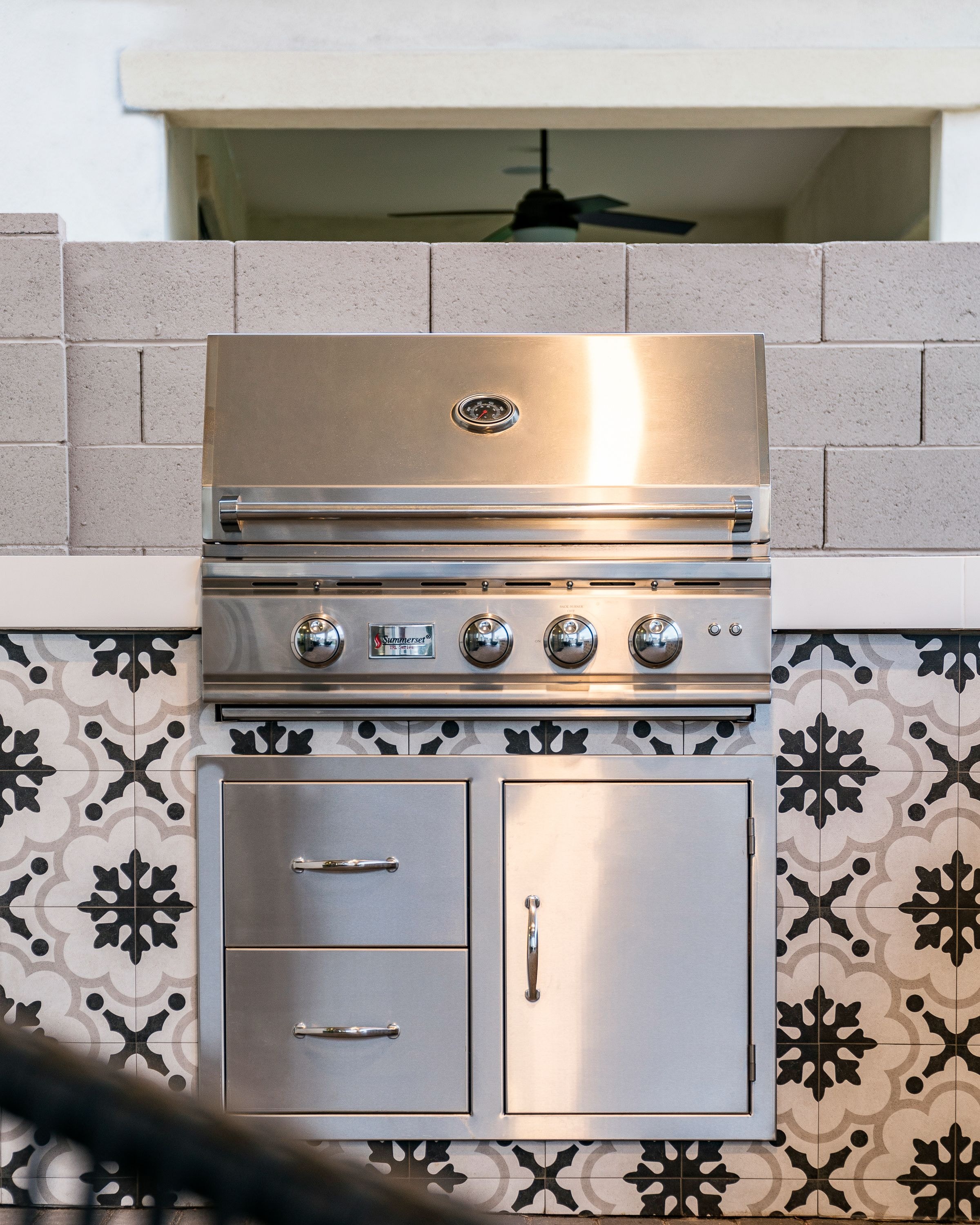 Stainless steel outdoor BBQ grill set into decorative black and white patterned tile surround