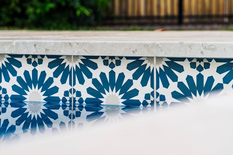 Close-up of blue and white geometric pool tile with travertine coping